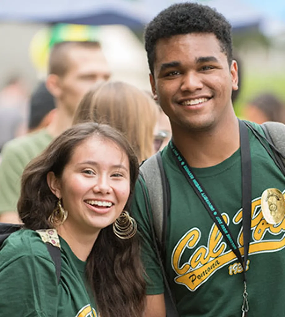 two students wearing Cal Poly Pomona t-shirts smile brightly at the camera during a student event.